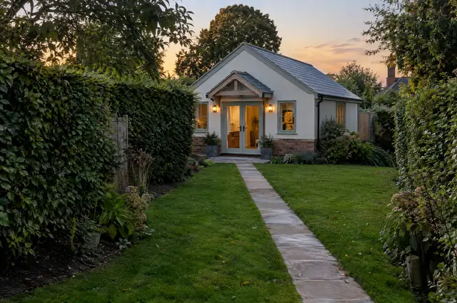 Rendered single-storey garden annexe with slate roof and French doors at the end of a garden
